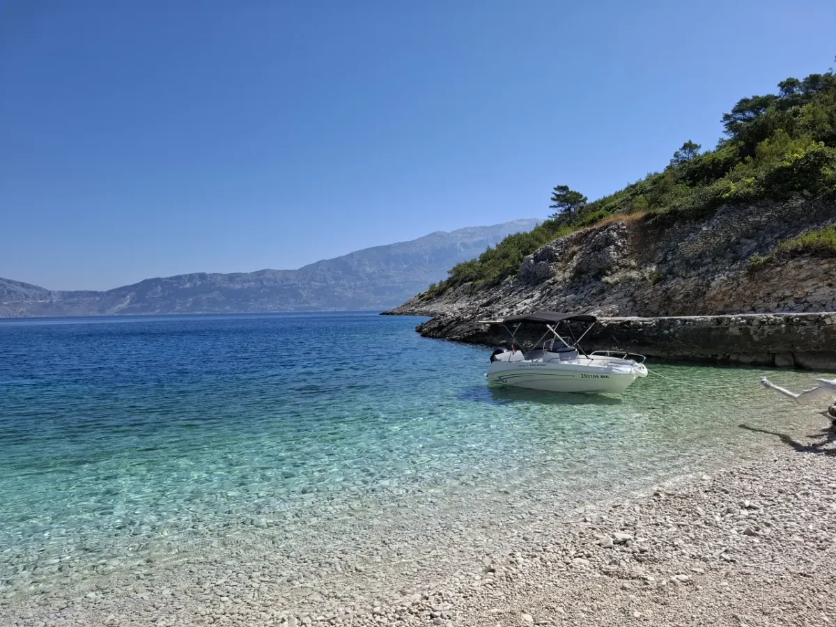 Boat moored by a white pebble beach in a secluded cove on Brač