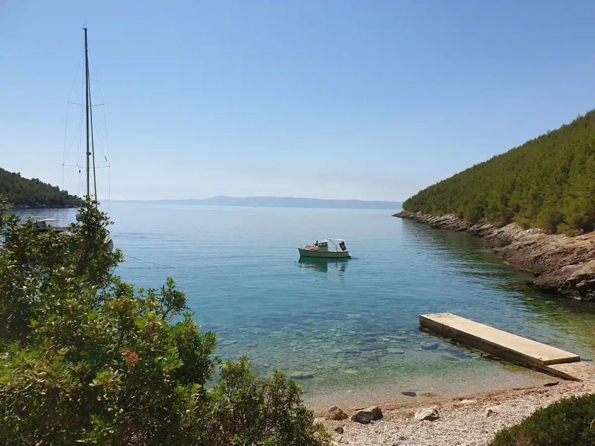 Sailboat anchored in a calm green bay with a stone pier on eastern Brač